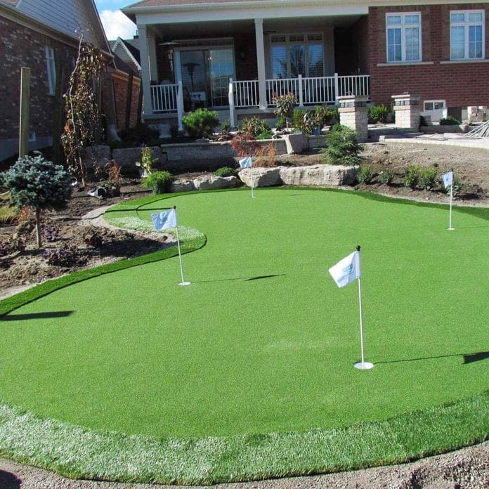 A backyard with a putting green and a lawn.